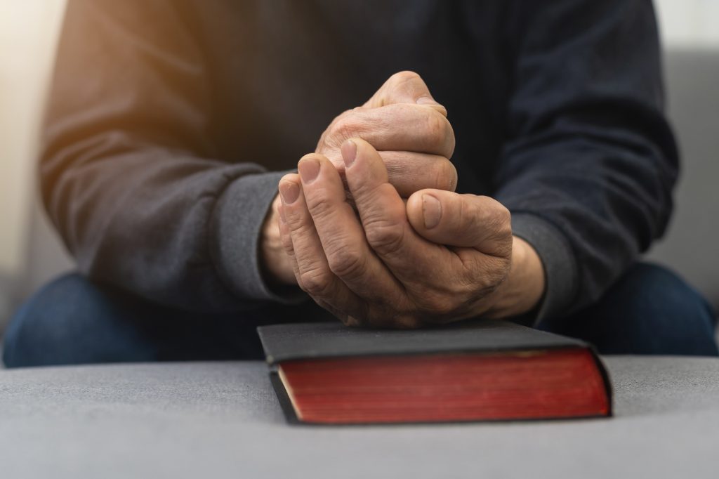 Please, Lord. Nervous worried aged Caucasian man praying on couch at home. Stressed white European