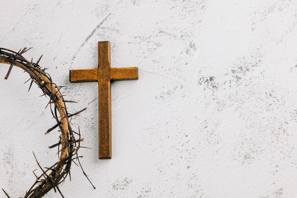 Wooden cross within a crown of thorns on light textured background for Palm Sunday.